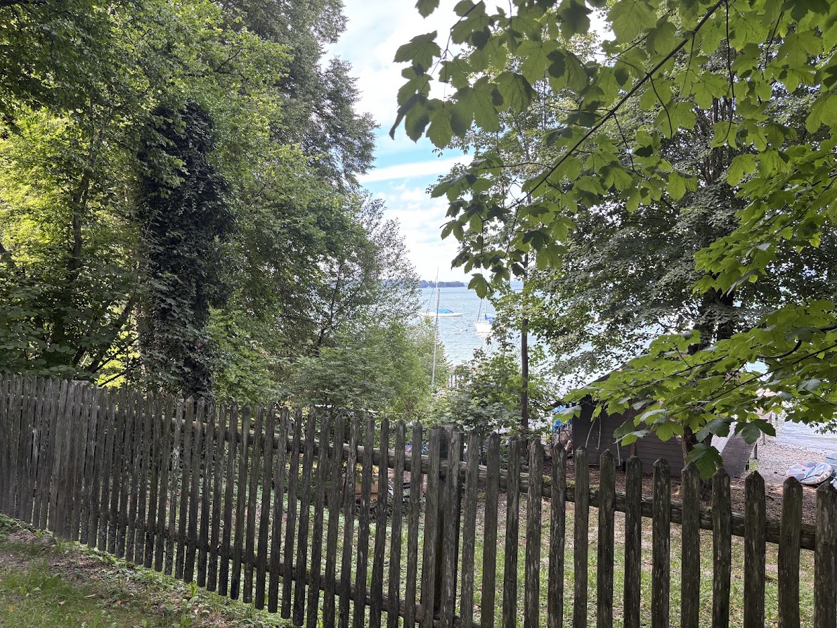 Blick durch Bäume und Gartenzaun auf den Starnberger See